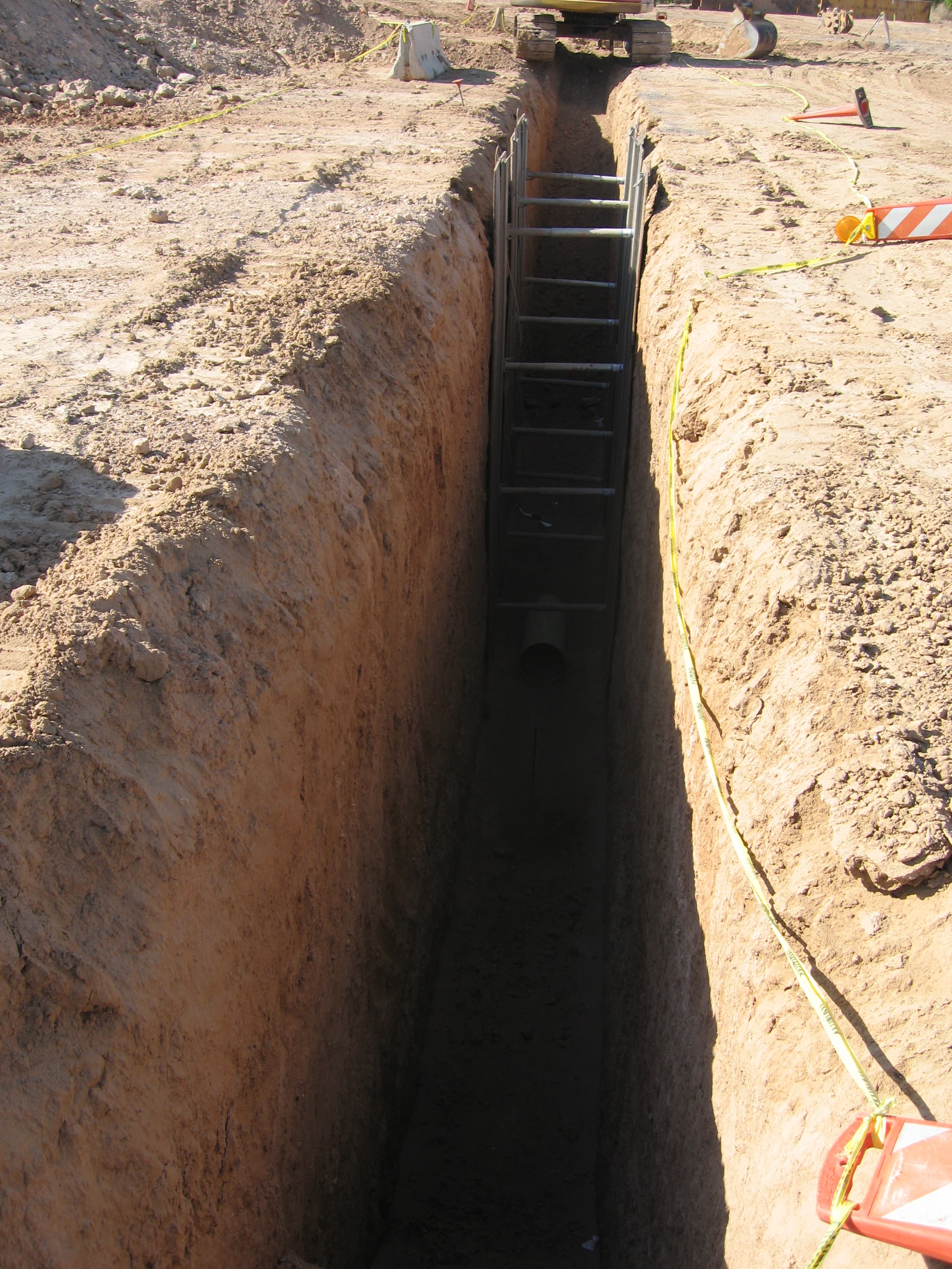 Looking down a deep utility trench with shoring and caution tape